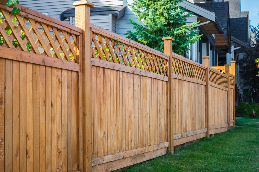 Nice wooden fence around house. Wooden fence with green lawn. Street photo A gardener wearing a blower walks along a lush, tree-lined path in a city park.